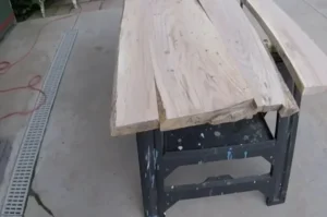 Rough live edge wood slabs laid side by side on a black steel workbench outdoors, before flattening and finishing