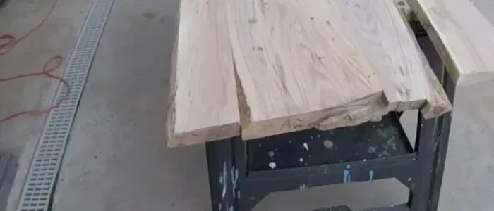 Rough live edge wood slabs laid side by side on a black steel workbench outdoors, before flattening and finishing