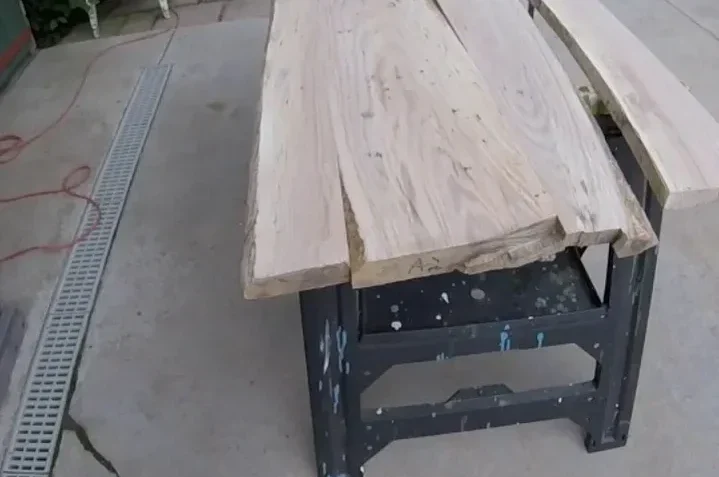 Rough live edge wood slabs laid side by side on a black steel workbench outdoors, before flattening and finishing